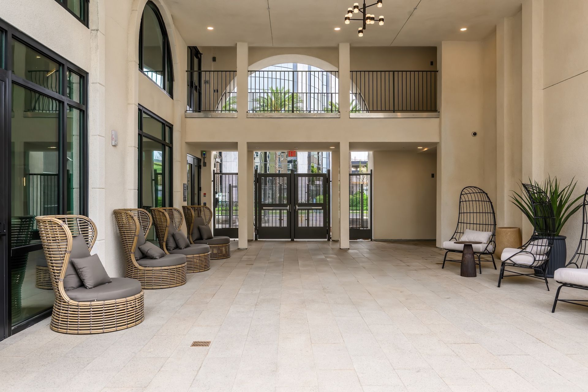 Covered outdoor lounge with wicker chairs, potted plants, and arched doorway.
