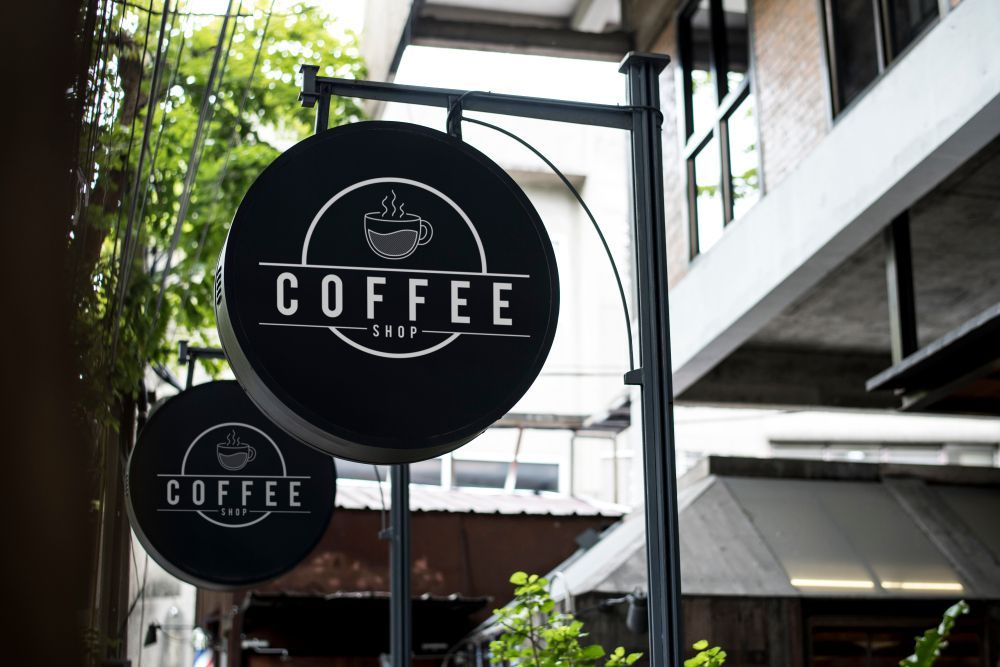 Two Signs For A Coffee Shop Are Hanging Outside Of A Building — JW Signs and Designs In Cloncurry, QLD