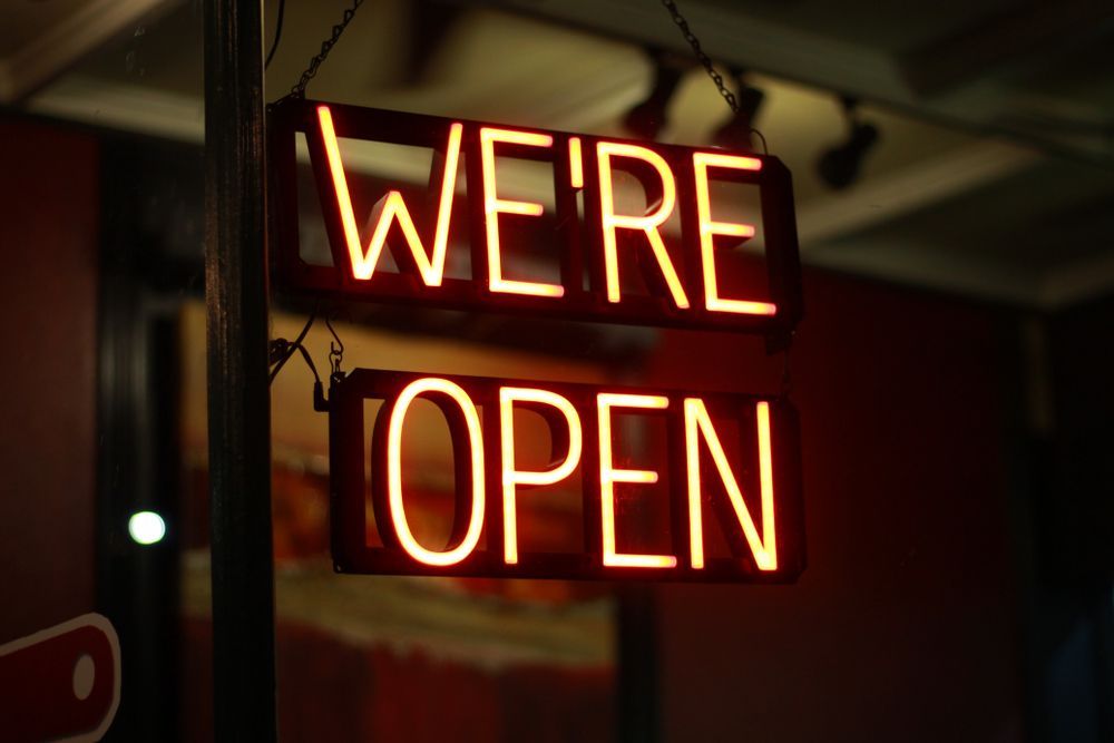 A Neon Sign That Says We 're Open Is Hanging From A Pole — JW Signs and Designs In Brisbane, QLD