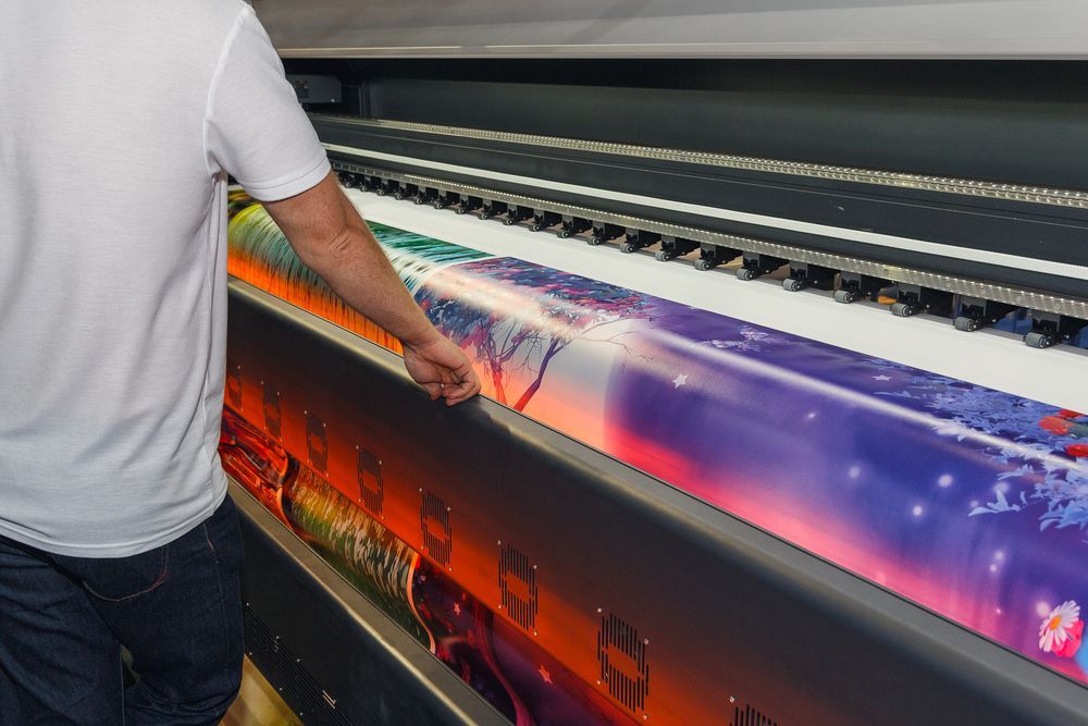 A Man Is Standing In Front Of A Large Printing Machine — JW Signs and Designs In Emerald, QLD
