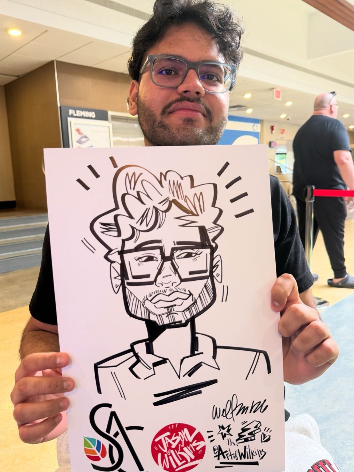 Fleming College guest with glasses holding his personalized live caricature by Jason Wilkins.