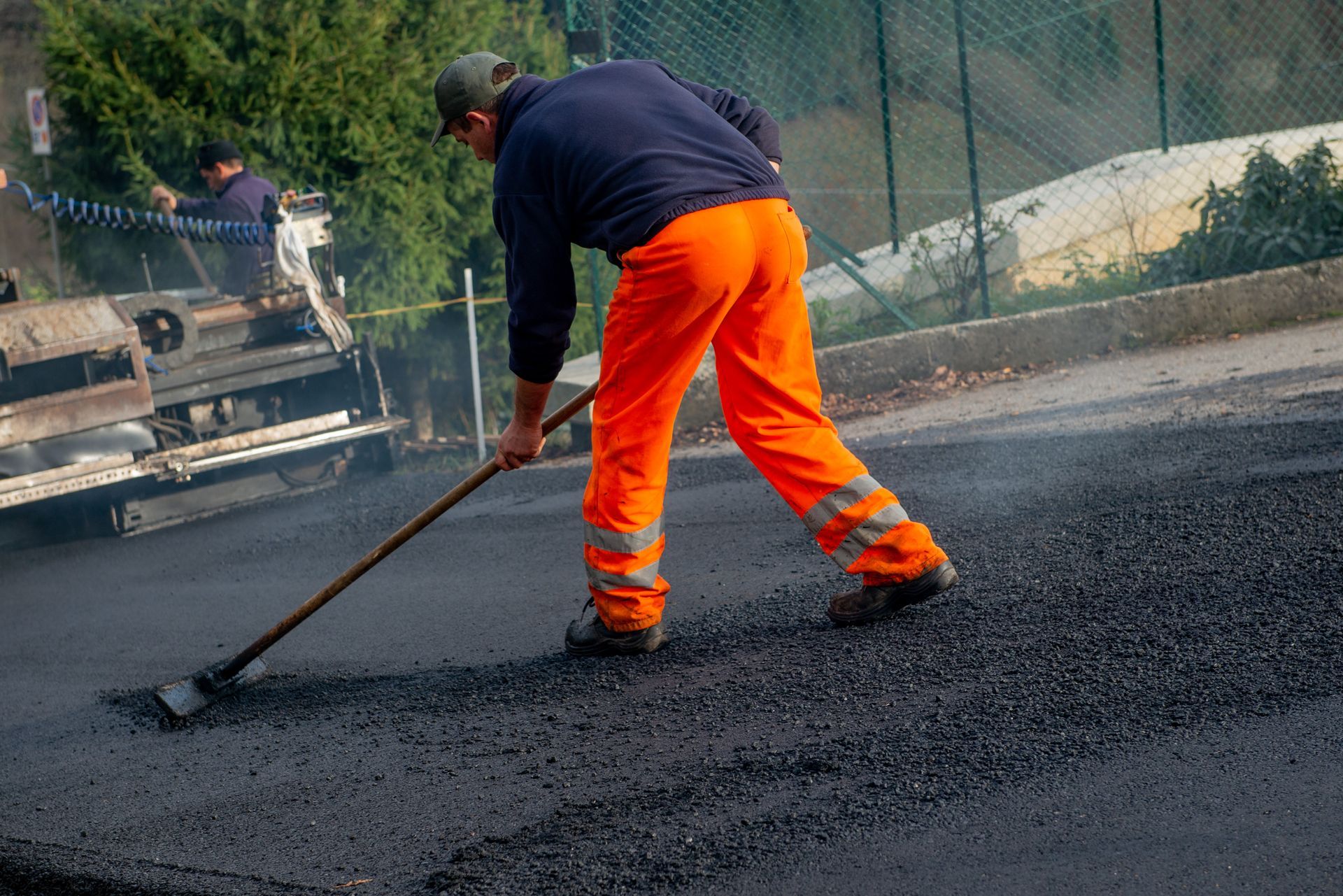 Worker raking fresh hot asphalt during a paving project with paver machine. Worker raking fresh hot asphalt during a paving project with paver machine.