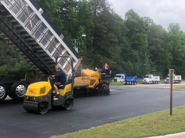 Asphalt paving in progress: truck dumping asphalt into a paver, compacting with a roller.