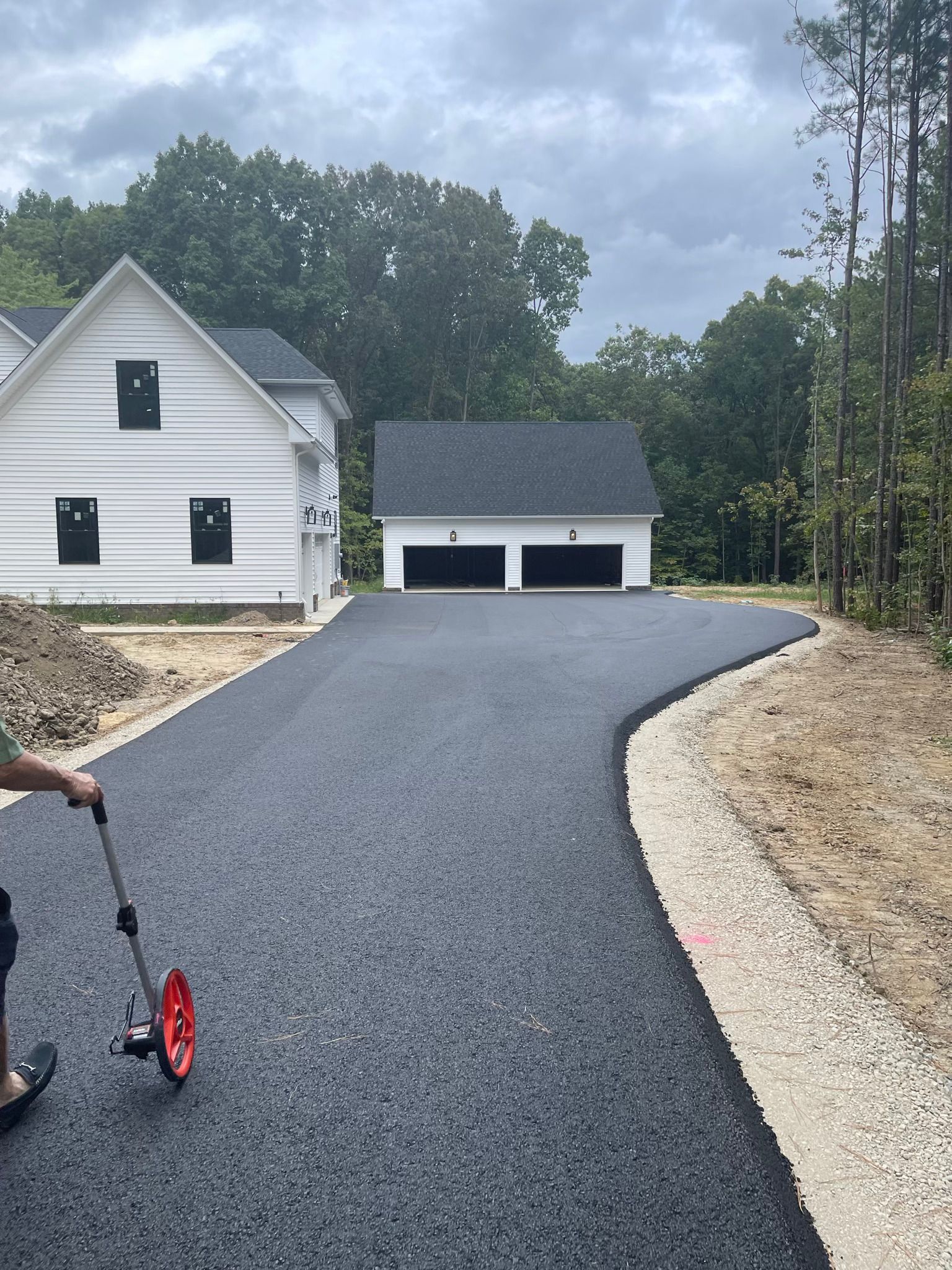 Newly paved asphalt driveway leading to a white house and garage, person using a measuring wheel.