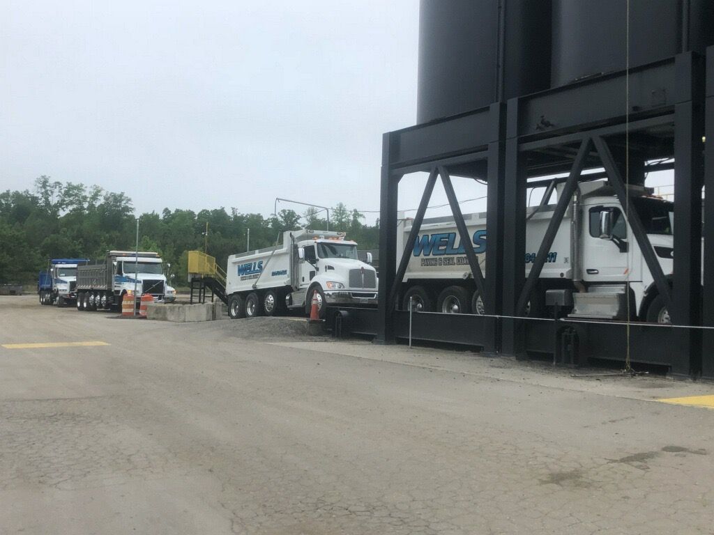 Trucks lined up at industrial loading area; dark silos in the background.