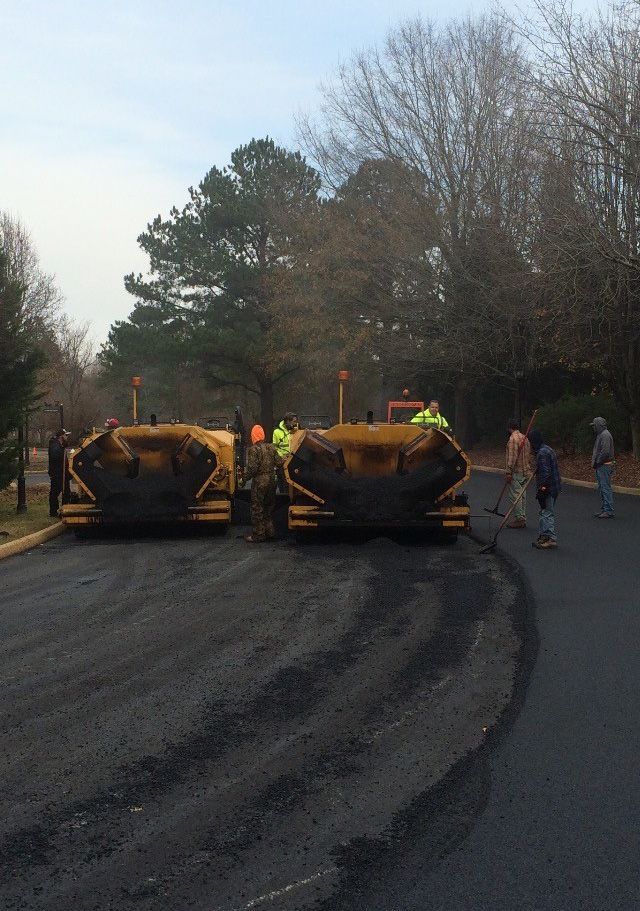Two asphalt pavers lay fresh blacktop; construction workers nearby.