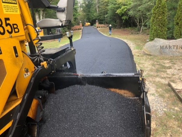Asphalt being laid on a curved pathway by a yellow paving machine. A person stands further down the path.
