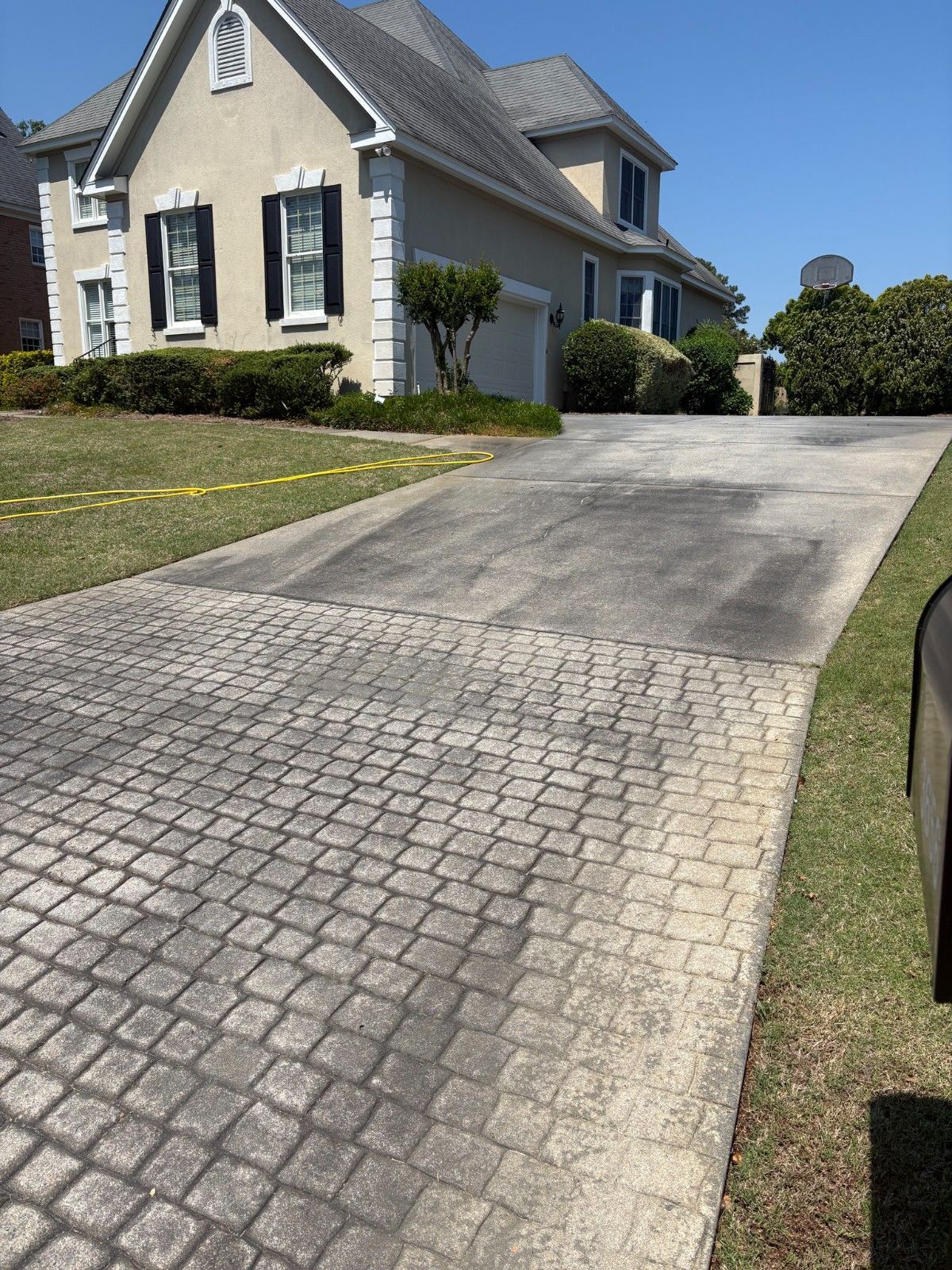 Driveway leading to a cream-colored house with black shutters and a manicured lawn.