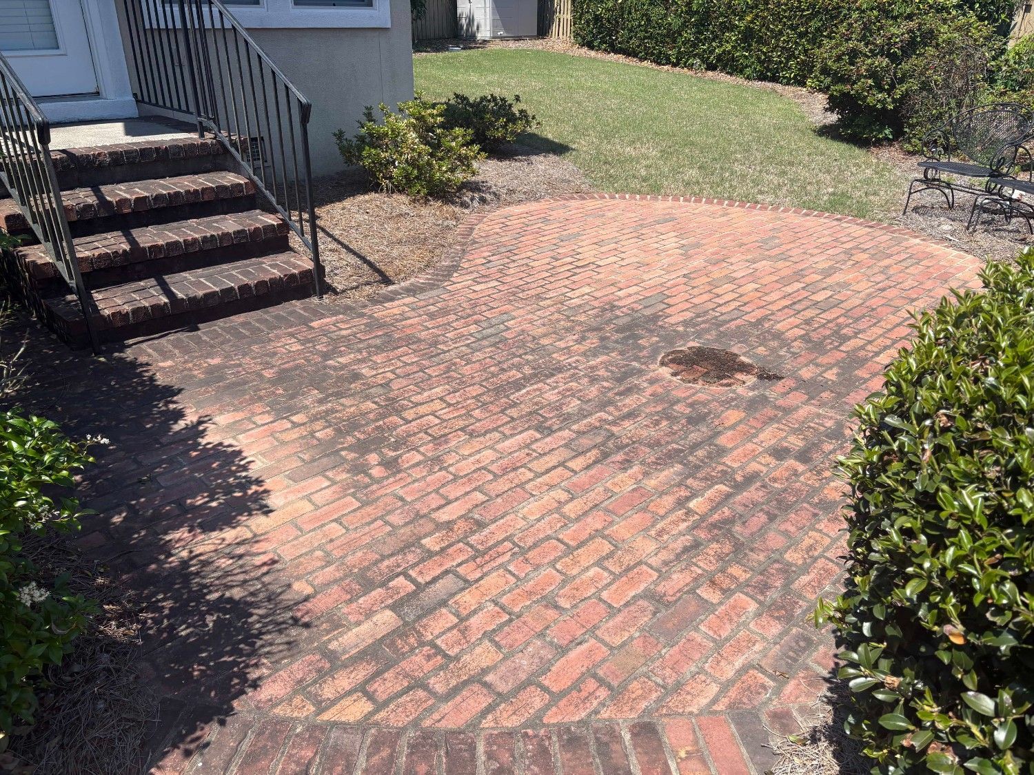 Brick patio beside house steps, with bushes and a grassy yard in bright sunlight