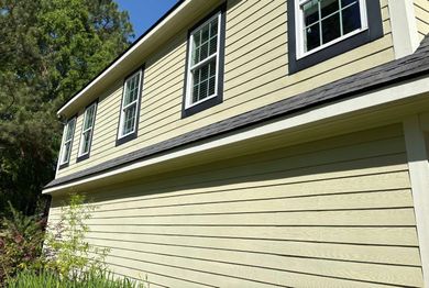 Side of a beige house with white-trimmed windows and sunlight on the siding