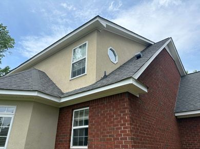 Two-story brick house with tan siding, gray roof, and a round attic window under a blue sky