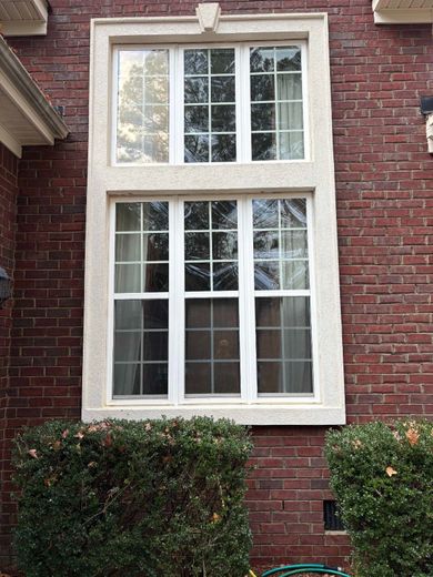 Tall white-trimmed window set in a red brick wall, with shrubs below.