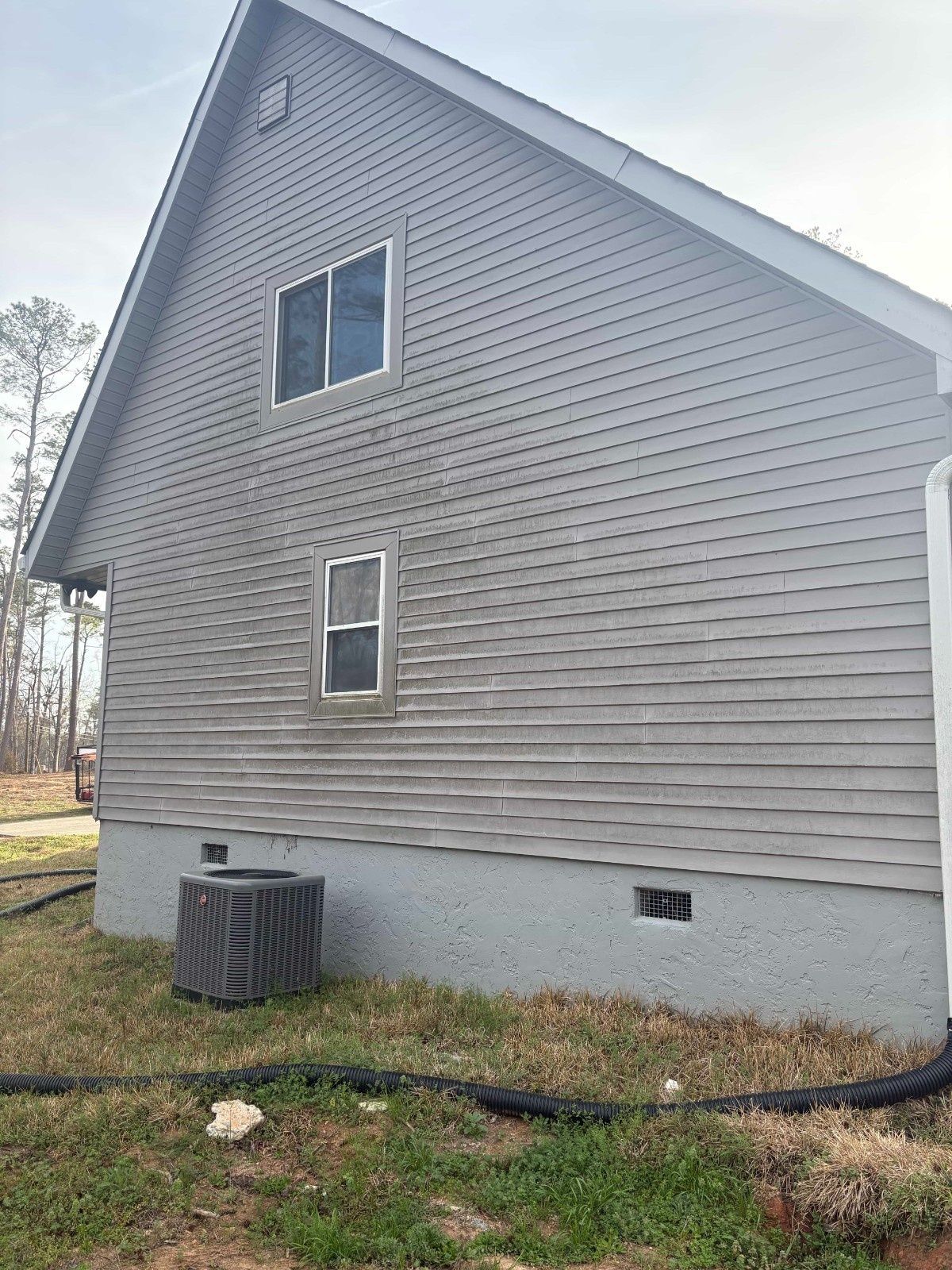 Gray house exterior with two windows, white foundation, and black cable along the ground