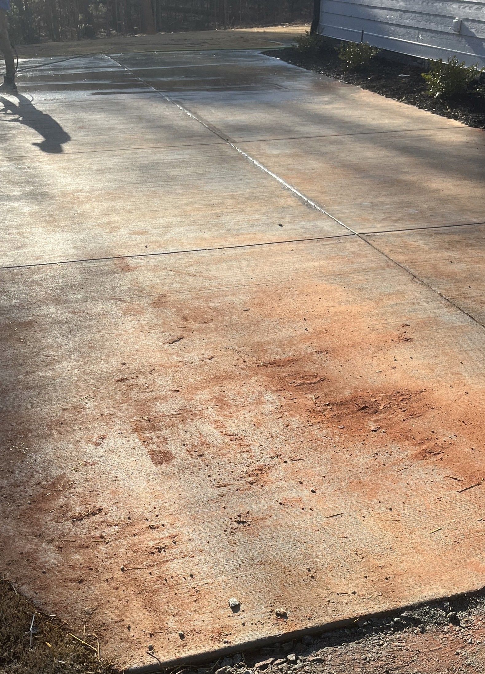 Concrete driveway with orange rust stains and scattered debris in sunlight