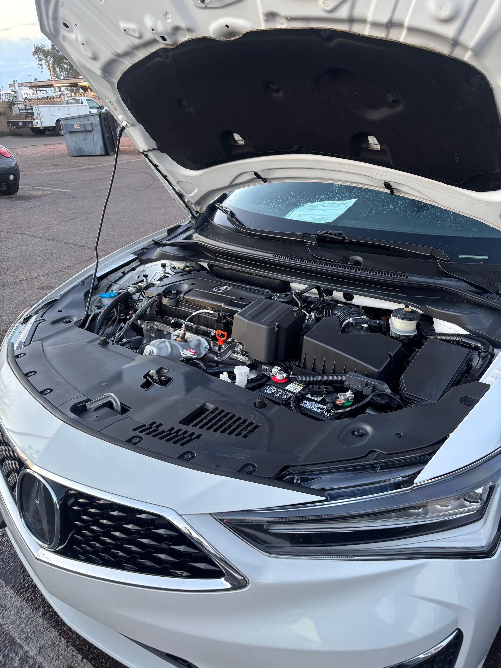 White car with hood open, showing the engine bay in a parking lot.