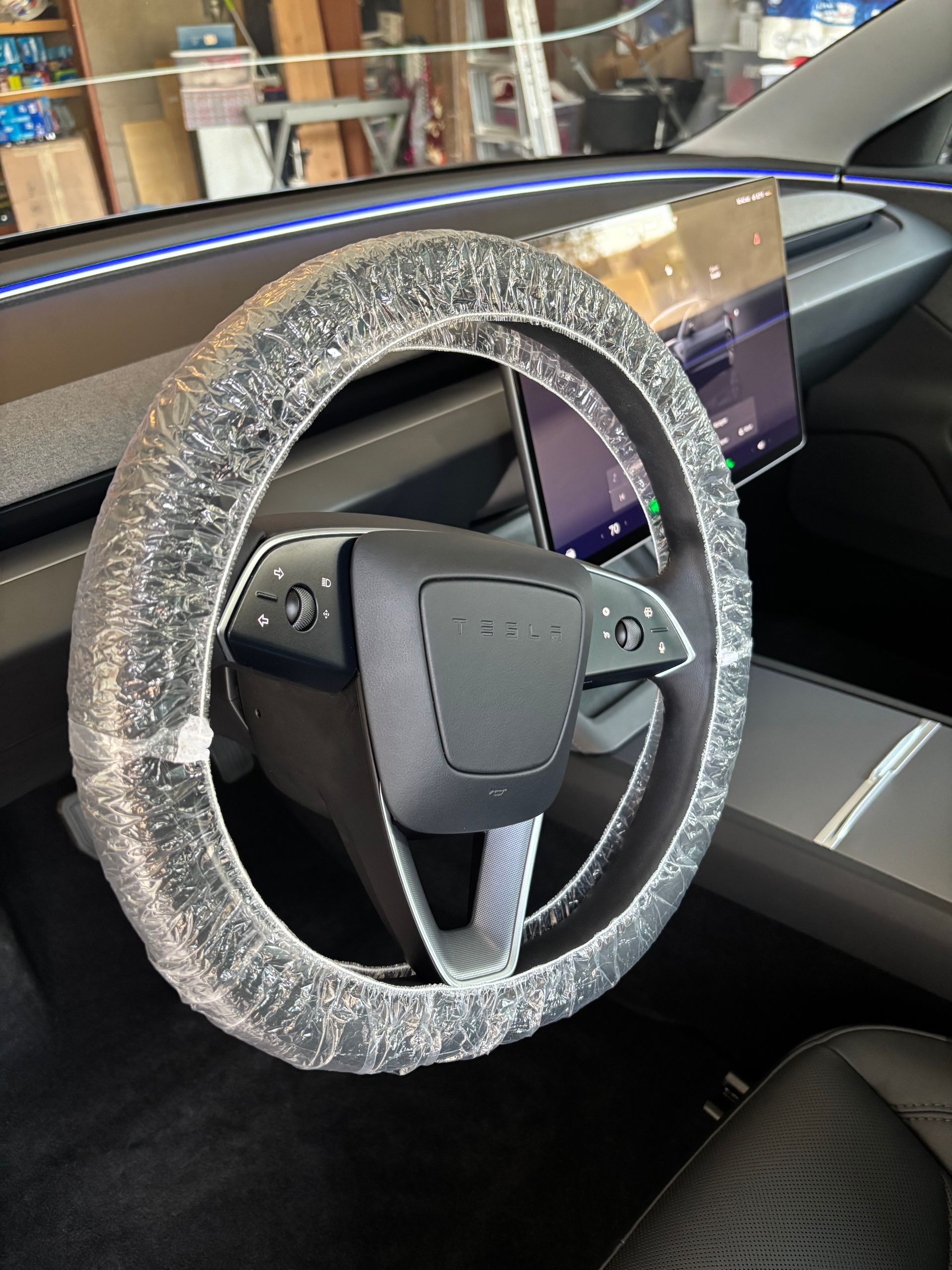 Car dashboard with a steering wheel covered in clear protective plastic and a large center display.
