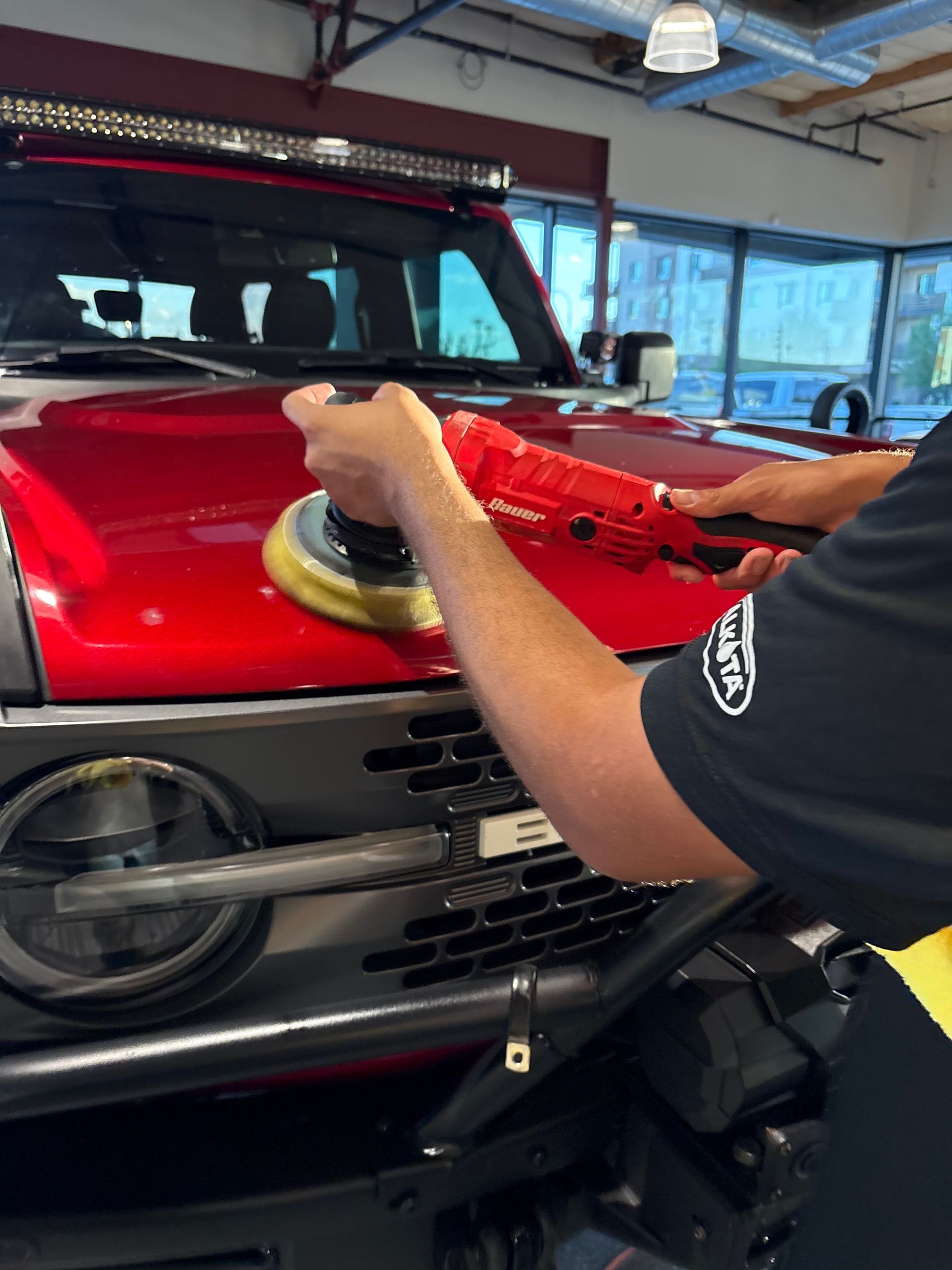 Technician polishing a red SUV hood in a garage, using a buffer tool