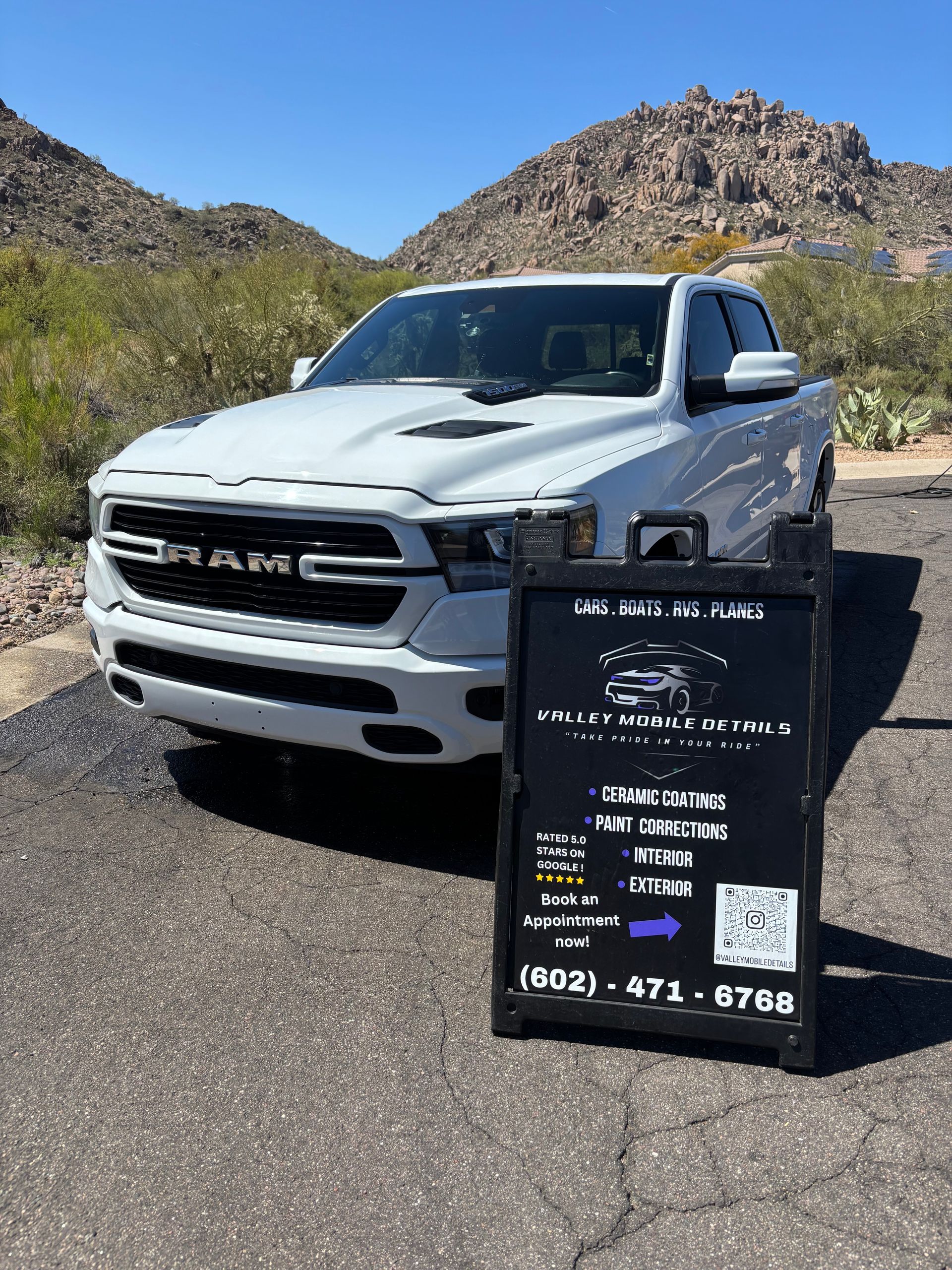 White Ram truck parked on a desert road beside a black real-estate sign with mountains in the background