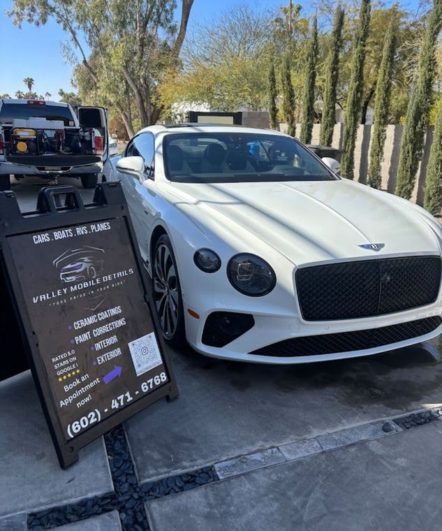 White Bentley parked beside a black menu sign on a sunny street