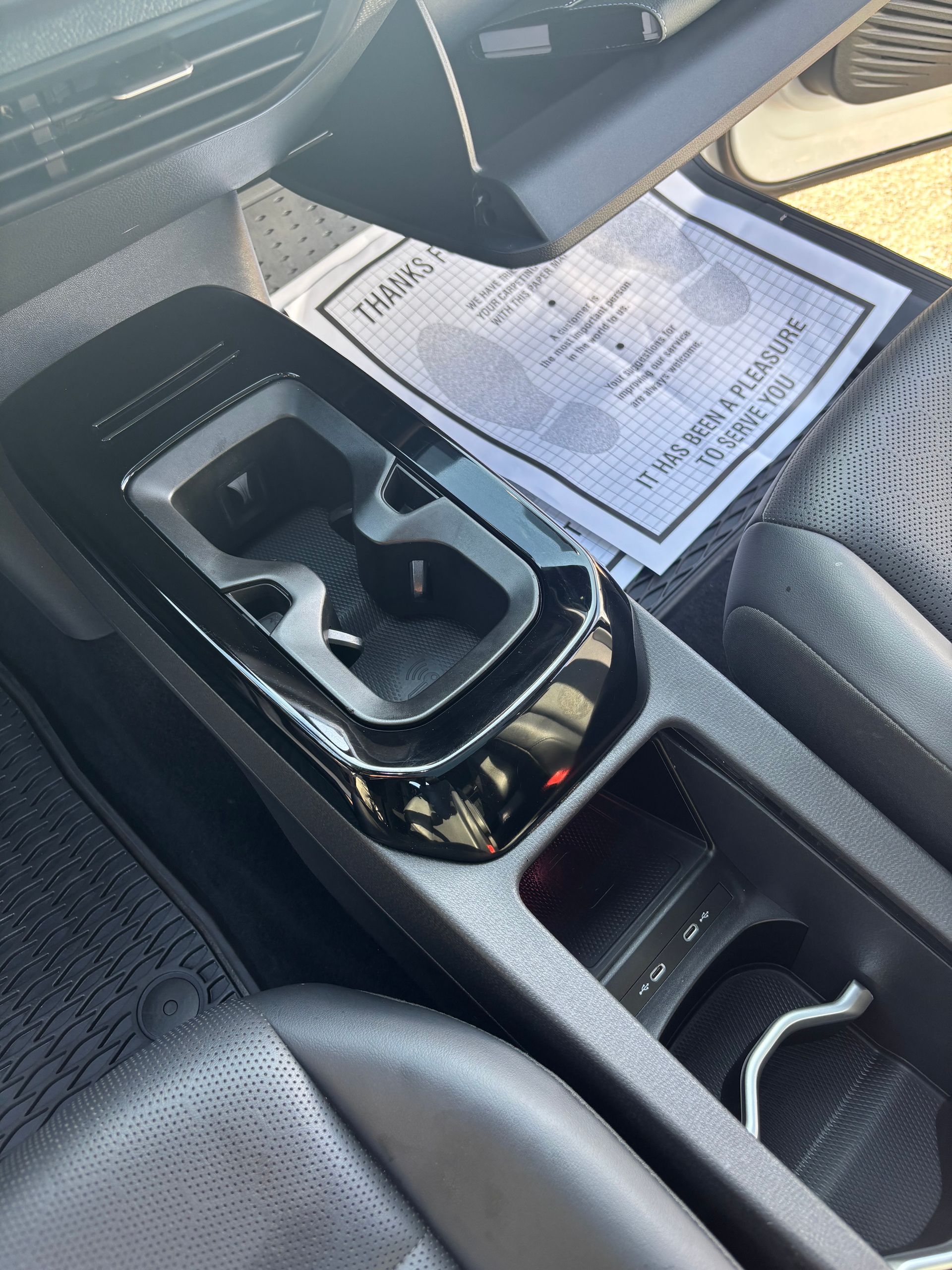 Car’s center console with cup holders and a printed document on the passenger seat.