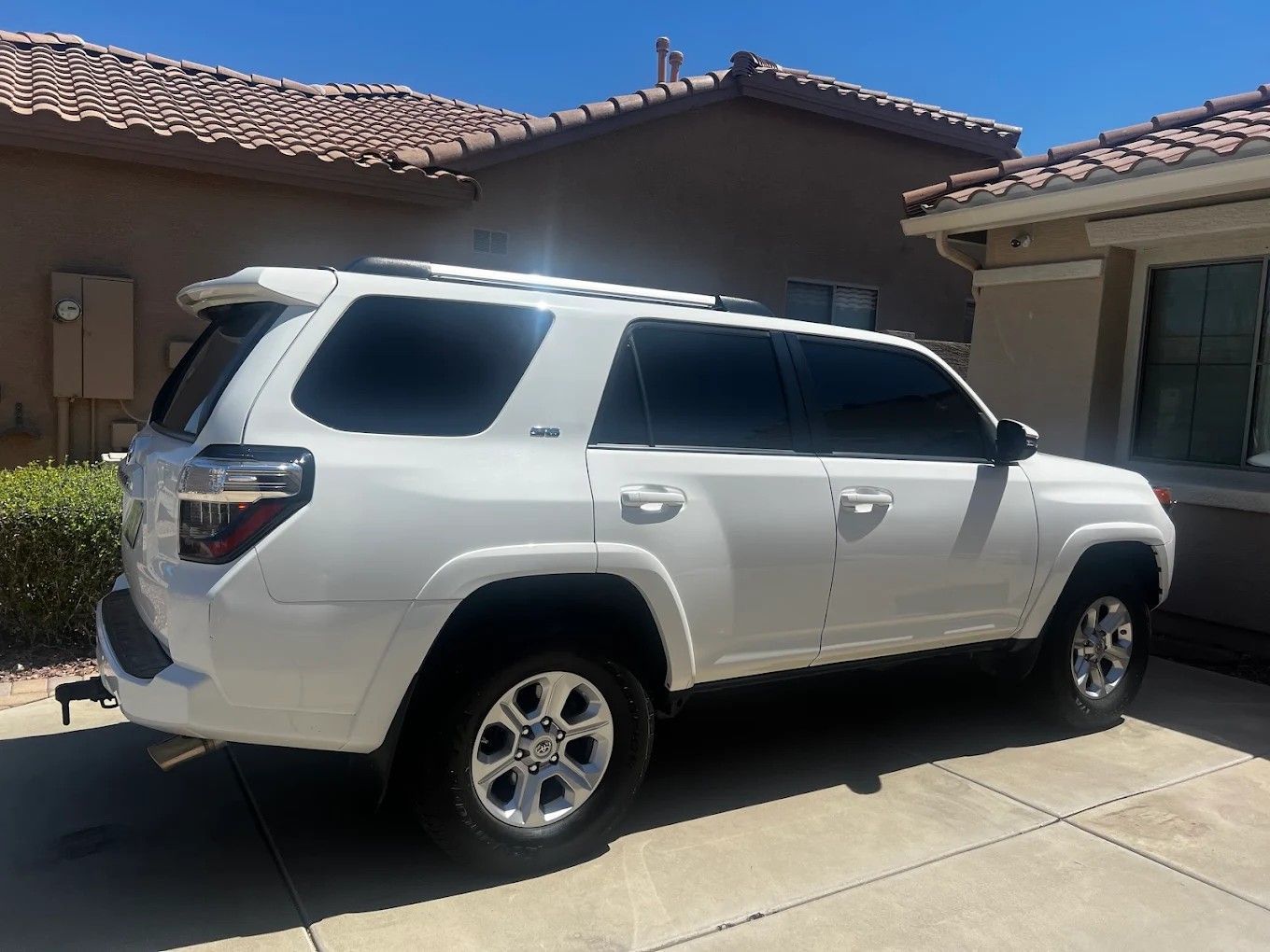 White SUV parked in a driveway beside a tan house on a sunny day