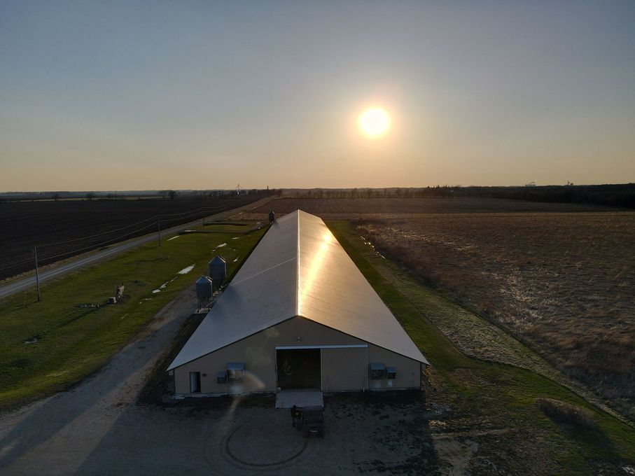 An aerial view of a large white building in a field at sunset.