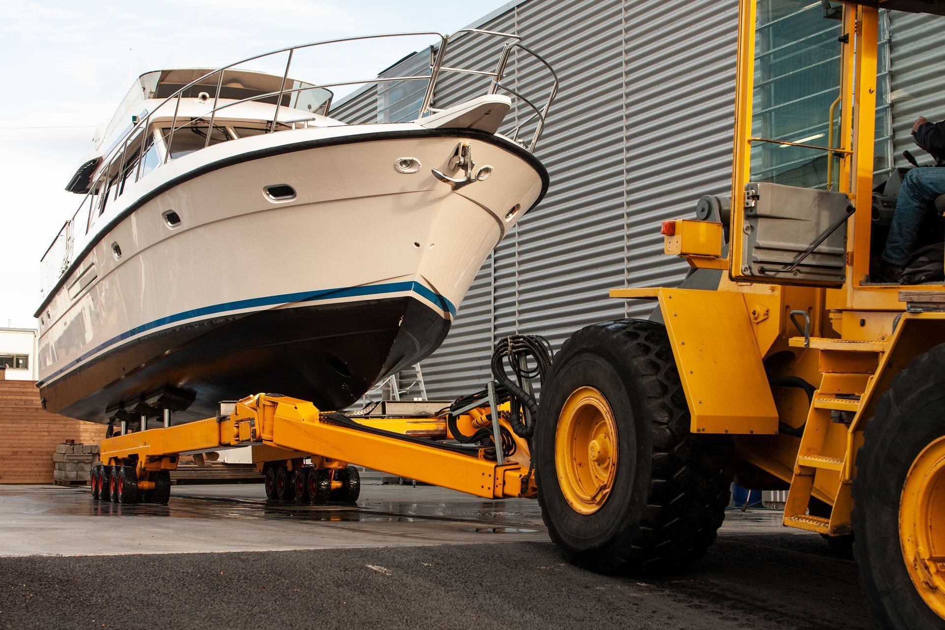 Yellow forklift moving a white yacht in an industrial yard