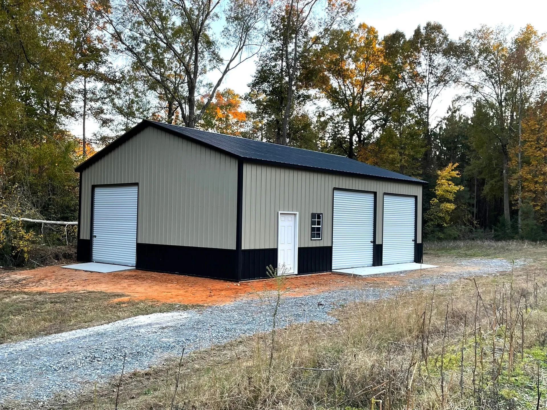 A large metal building with two garage doors is sitting in the middle of a field.