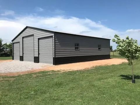A large metal garage is sitting in the middle of a grassy field.