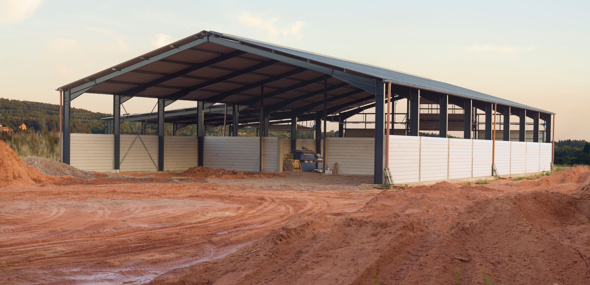 A large metal building is being built in a dirt field.