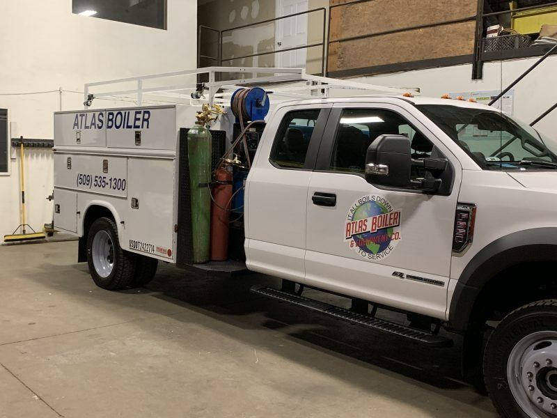 A white Atlas Boiler utility truck with a crane rack parked inside a warehouse.