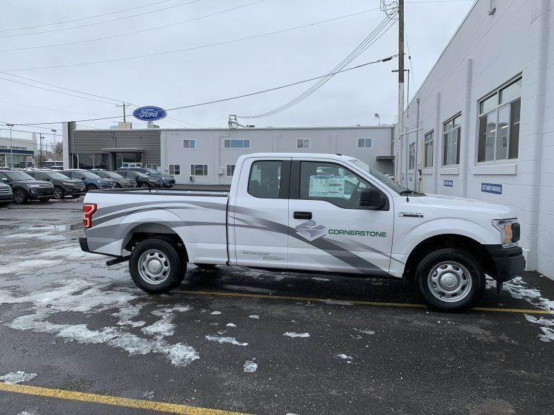 White Ford pickup truck with gray side decals parked in a snowy car dealership lot.