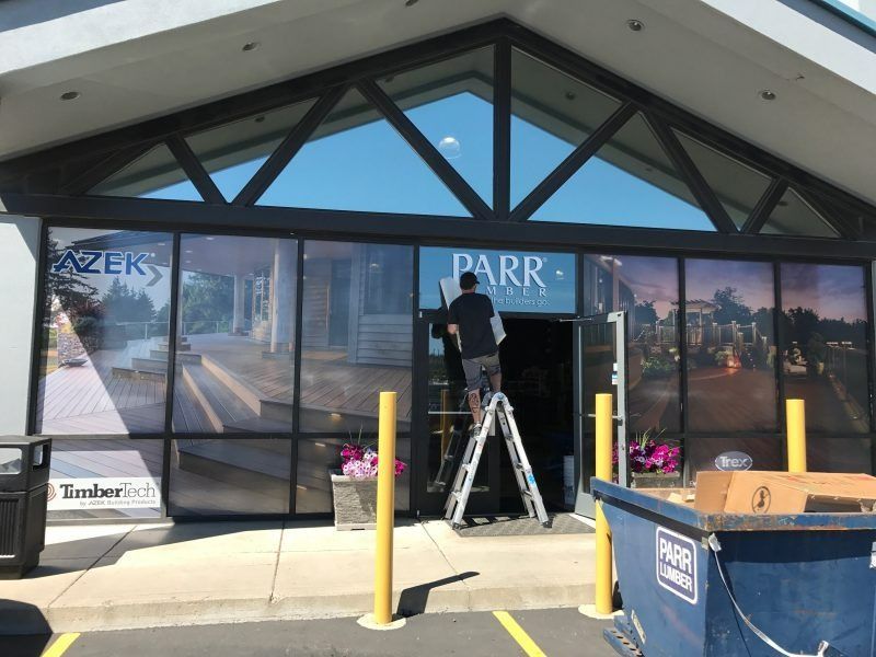 A worker on a ladder installs signage on the glass front doors of a Parr Lumber building.