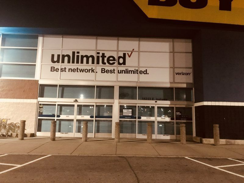 Entrance to a Best Buy store at night, featuring a large Verizon 
