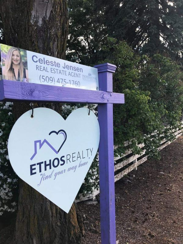 A purple real estate sign with Celeste Jensen's contact info above a heart-shaped Ethos Realty logo by a tree and fence.