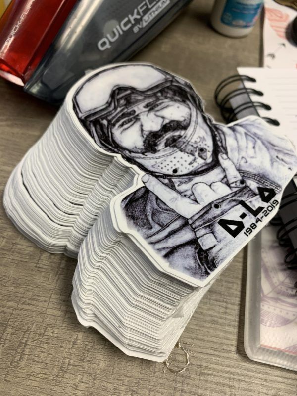 A stack of stickers featuring a black-and-white ink illustration of a person wearing a helmet, giving a peace sign.