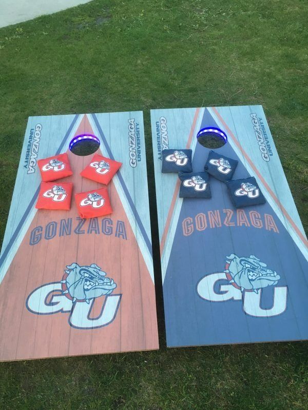 Two Gonzaga-themed cornhole boards set on grass, one orange and one blue, with four matching beanbags on each.