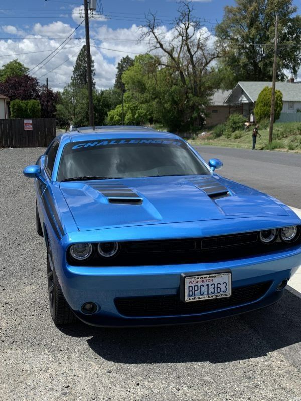 A bright blue Dodge Challenger parked on a gravel surface under a partly cloudy sky.