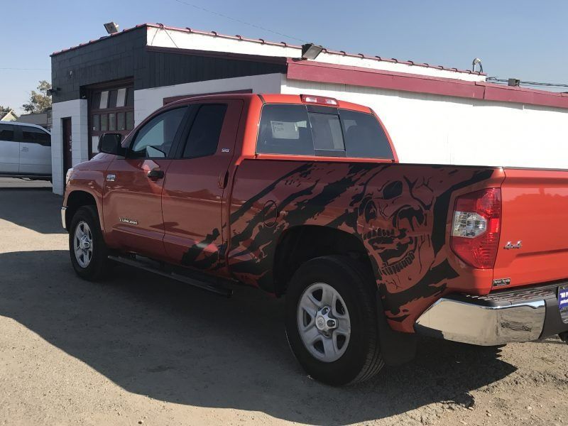 An orange pickup truck parked in front of a building, featuring a large black skull and claw mark decal on its side.
