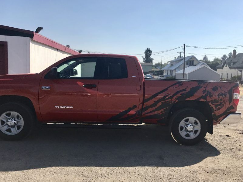 A red Toyota Tundra pickup truck with black claw-mark graphics on the rear quarter panel, parked on a gravel lot.