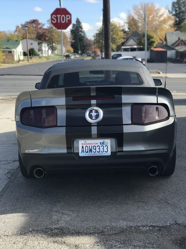 A silver Ford Mustang convertible with black racing stripes parked on a street in front of a red stop sign.