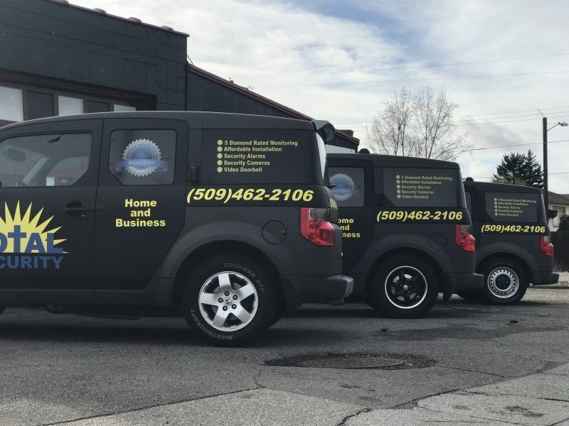 Three black Total Security company vans parked in a row outdoors.