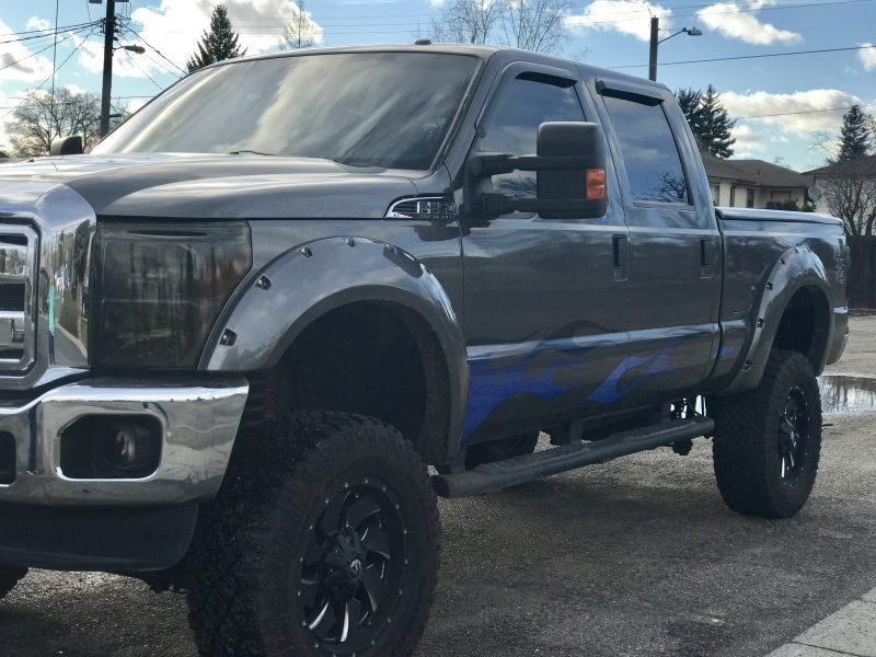 A lifted, charcoal-gray Ford Super Duty pickup truck parked on an asphalt surface during the day.