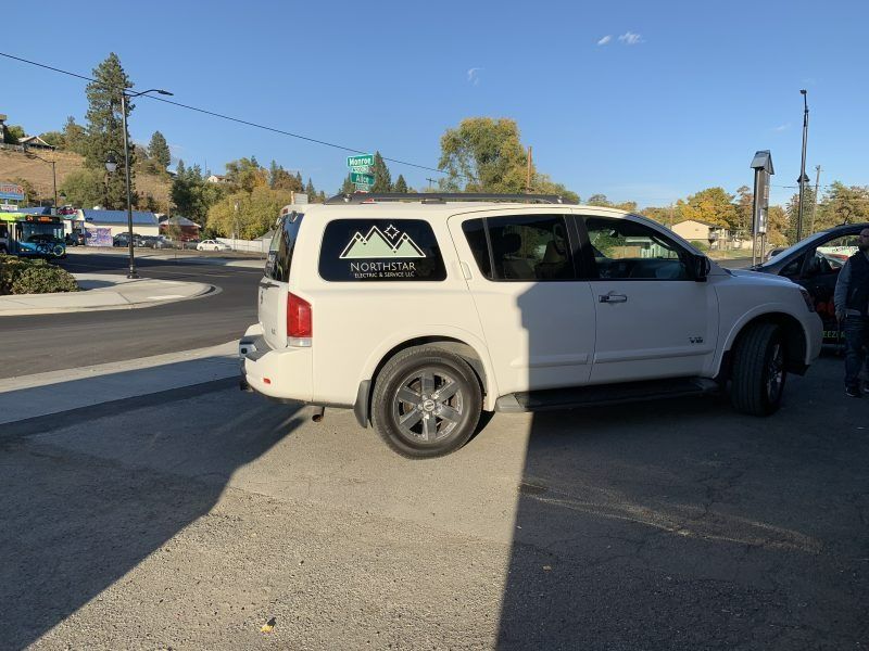 A white SUV parked on asphalt in an outdoor setting features a mountain logo and text on its rear side window.