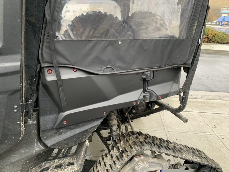 Side view of a black off-road vehicle with a soft enclosure and installed snow tracks.