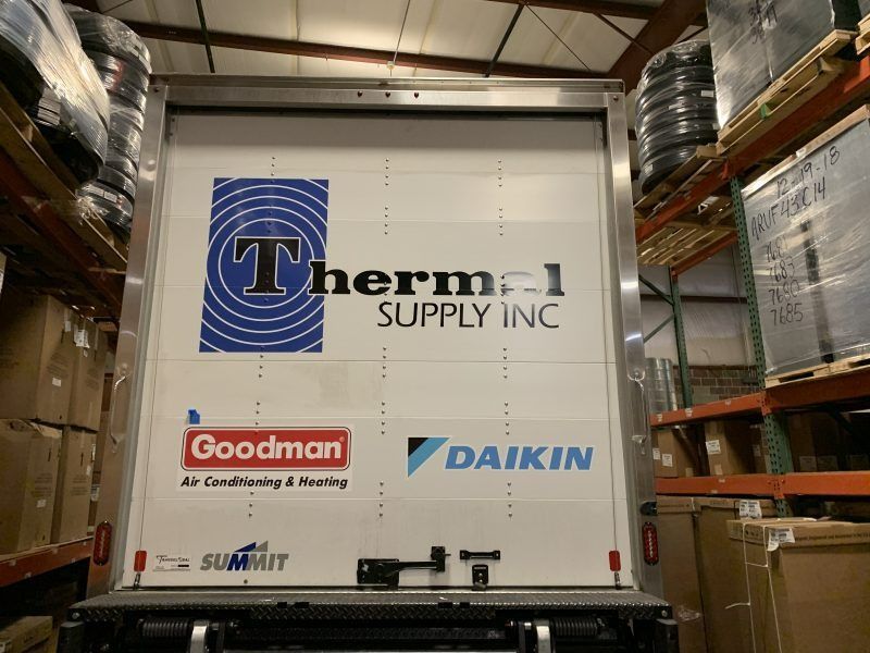 Rear view of a delivery truck in a warehouse, featuring the Thermal Supply Inc, Goodman, and Daikin brand logos.