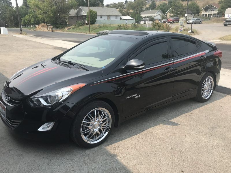 A black Hyundai Elantra with custom chrome wheels, tinted windows, and a red racing stripe parked on a street.