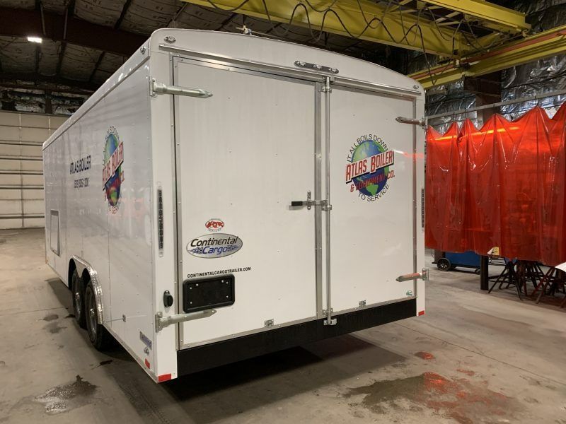A white enclosed cargo trailer parked inside an industrial facility with a red privacy curtain in the background.