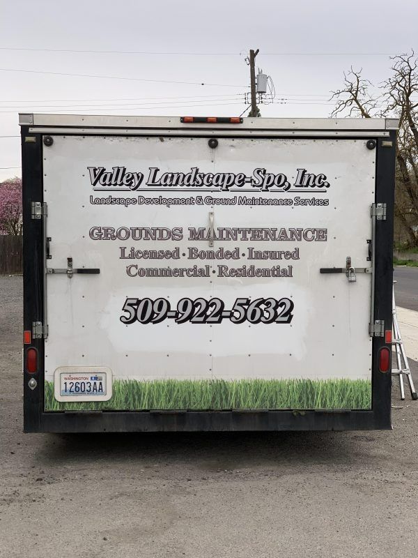 Back view of a white utility trailer for Valley Landscape-Spo, Inc., showing contact info, services, and a grass graphic.