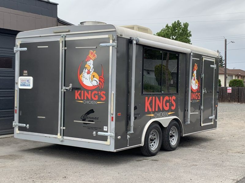 A grey King's Chicken food trailer parked outside, featuring a logo of a crowned chicken on the side and back doors.